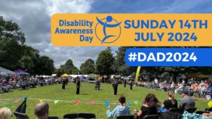 Image of people watching an event in a field with a text banner : Disability Awareness Day #DAD